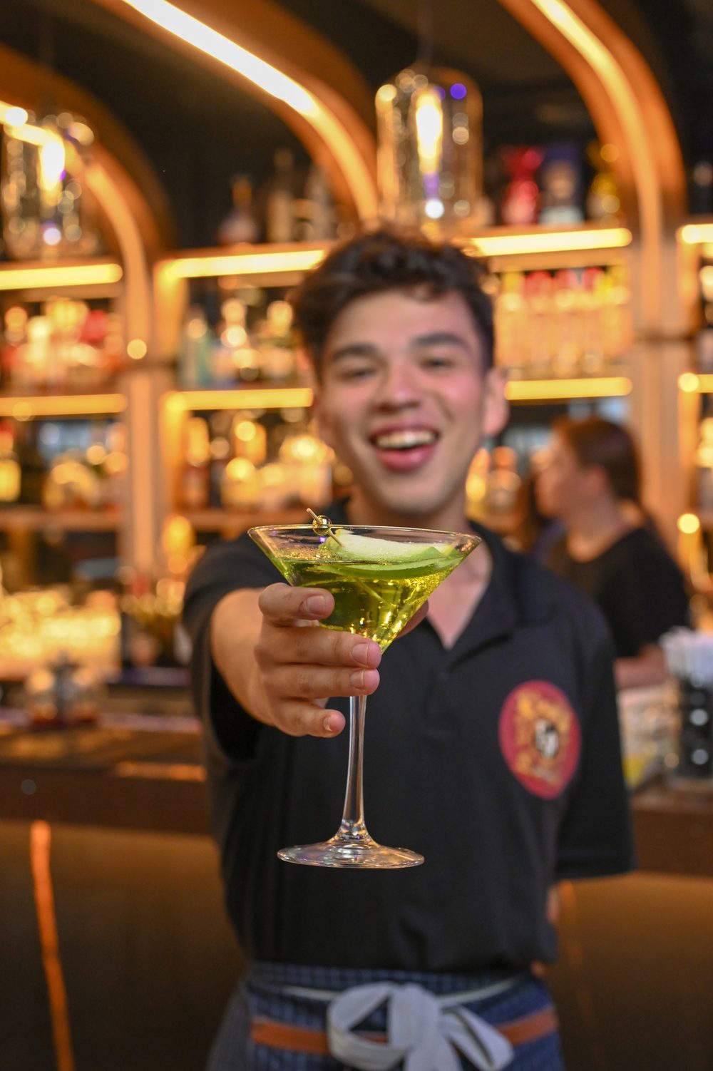 Smiling bartender offering a cocktail at the gold bar